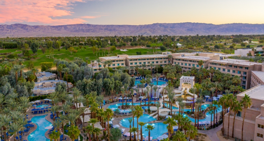 Aerial view of a desert resort with palm-lined pools at sunset