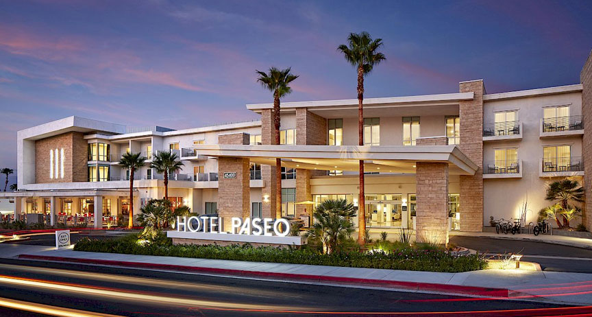 Hotel PASEO entrance lit at dusk with palms alongside