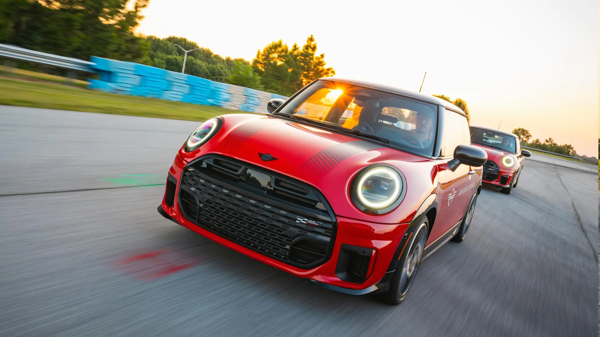 Two red MINIs cornering nose to tail through a track corner at sunset