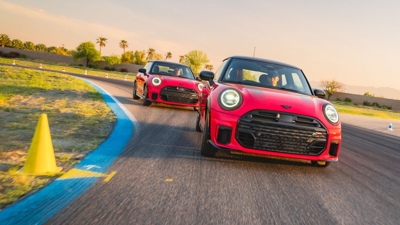 Two red MINIs cornering on the desert circuit past a line of palm trees