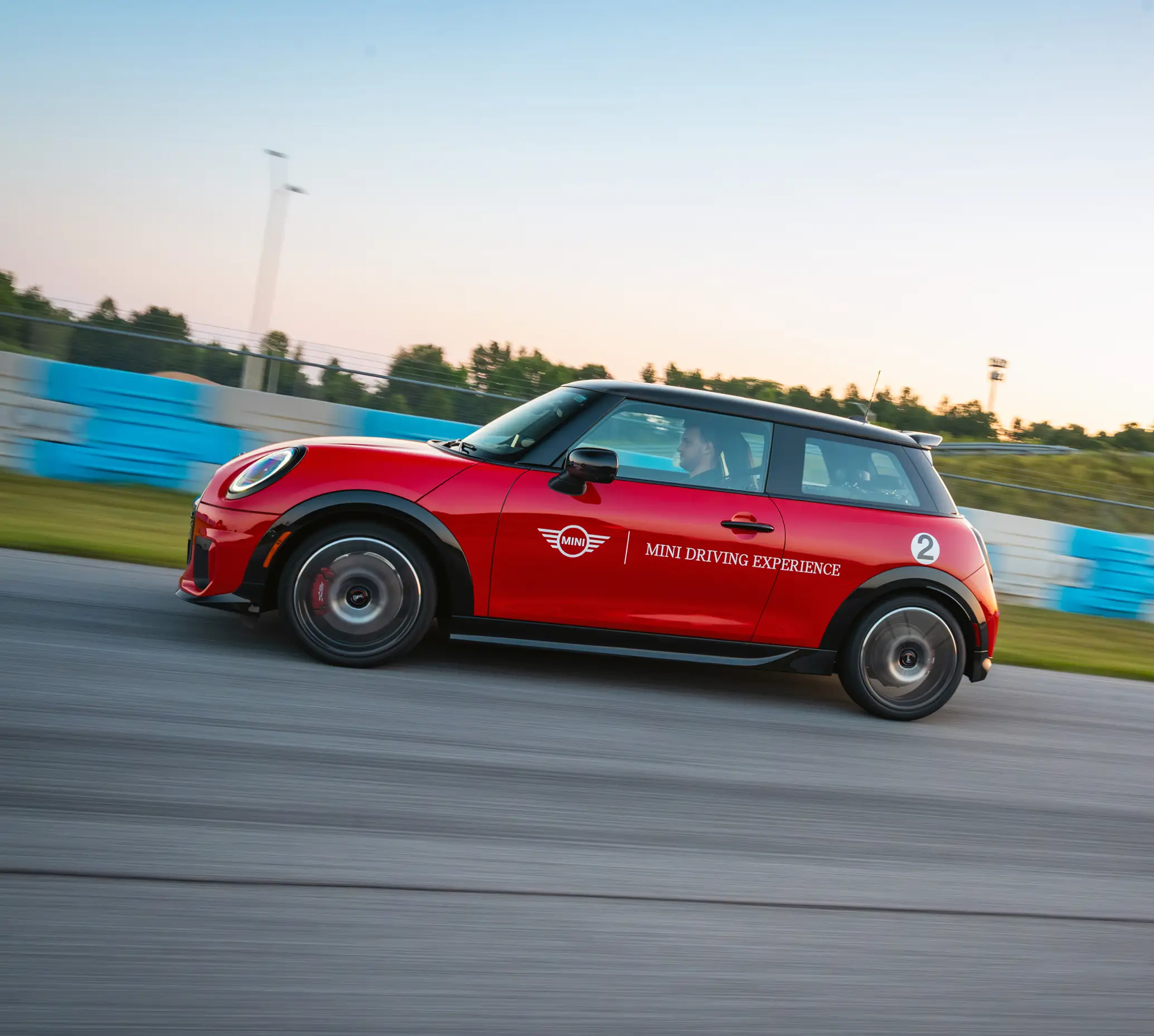 Red MINI Driving Experience car at speed past the blue track barriers